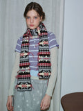 Woman poses with a long knit scarf adorned with ethnic-inspired motifs.