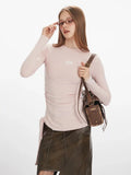 Model adjusting her glasses while wearing a light pink long-sleeve ruched top and a brown crossbody bag