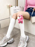 White knee-high socks with a pink plush bear charm and grey athletic shoes.