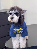 A Miniature Schnauzer dog wears a blue t-shirt with yellow 'Peanut Butter' text on the front.
