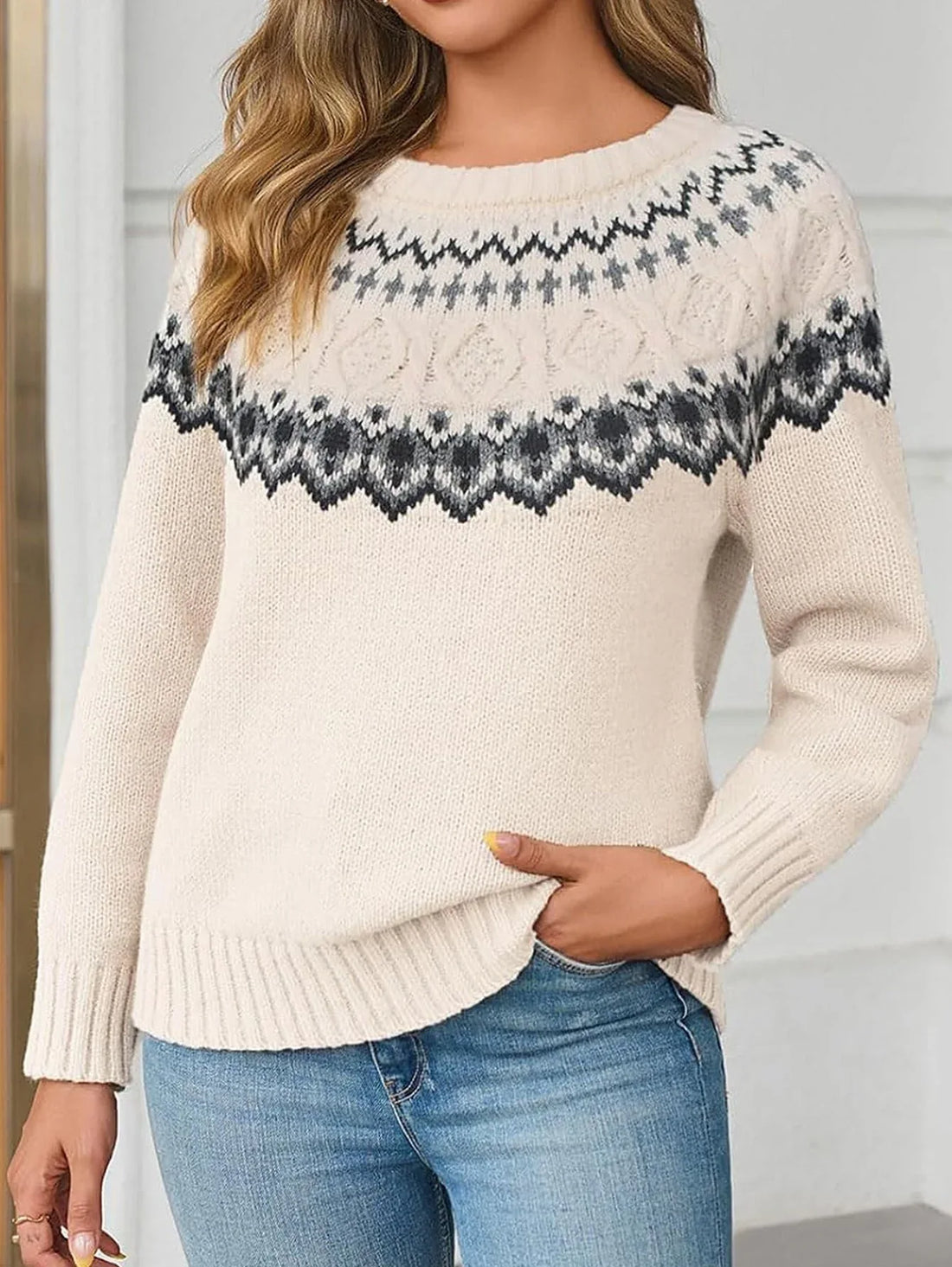 Woman wearing a cream-colored knit sweater with a black and grey Fair Isle pattern, paired with blue jeans.