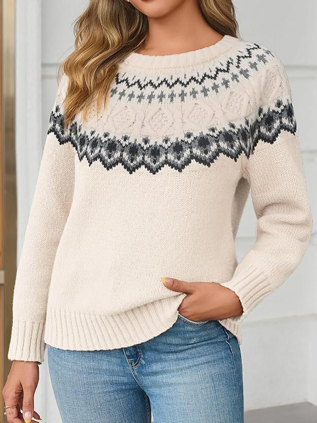 Woman wearing a cream-colored knit sweater with a black and grey Fair Isle pattern, paired with blue jeans.