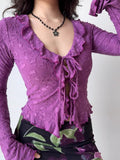 Woman's torso showing a purple textured mesh long-sleeve top with ruffled edges and a central tie detail.