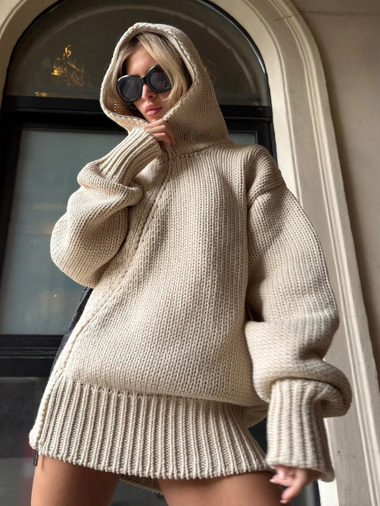 Woman wearing an oversized beige chunky knit hooded tunic sweater with ribbed trim.