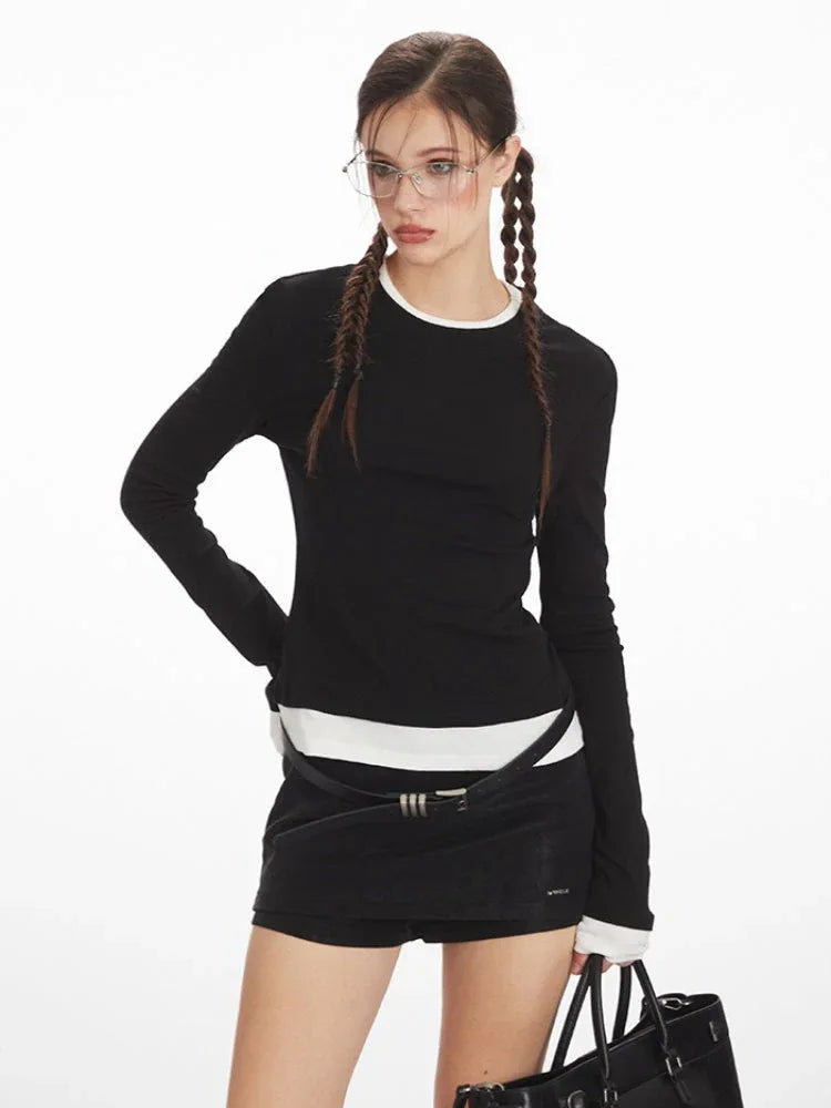 Close-up of a model wearing a black long-sleeve top with white contrast trim, styled with a belt and black shorts.