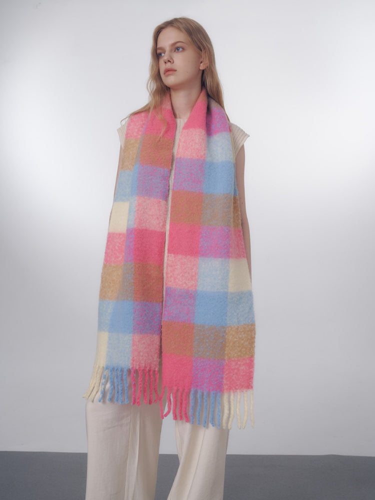 Woman wearing a long, oversized scarf with a pink, blue, and tan plaid pattern and fringed edges.
