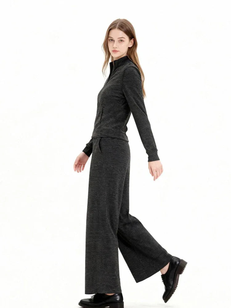 Woman wearing a charcoal grey knit loungewear set with a full zip jacket and wide leg pants, walking motion.
