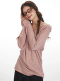 Woman wearing a dusty rose long-sleeve knit top with a V-neck, resting her head on her hands. She has braids and glasses.