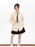 Woman wearing an oversized beige pinstripe button-down shirt with a brown plaid tie and a black skirt.