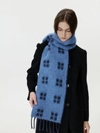 Woman adjusting a blue scarf with a black windowpane plaid pattern around her neck