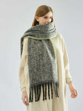 Woman modeling a winter scarf in grey with black fringe and green accent.