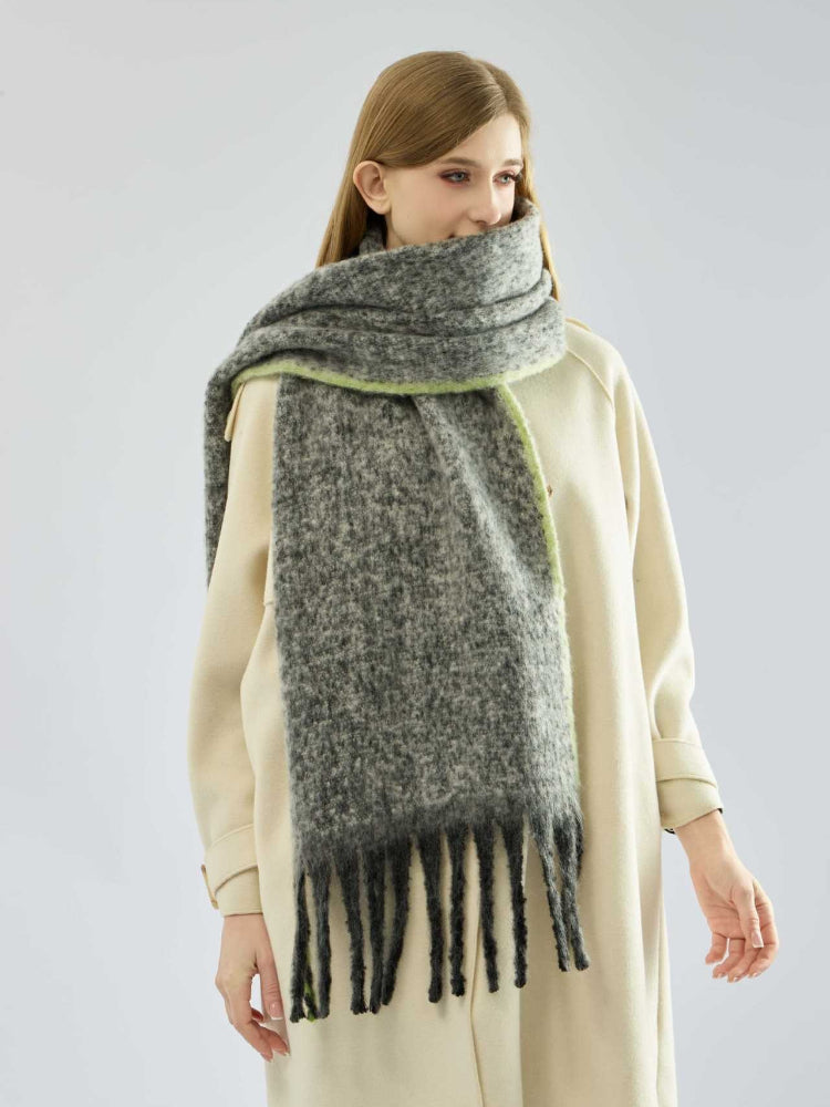 Woman modeling a winter scarf in grey with black fringe and green accent.