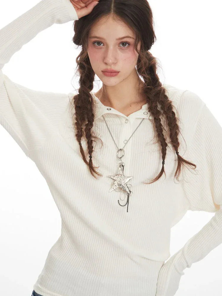 Detailed view of the neckline and embellished necklace on a woman wearing a white ribbed knit long-sleeve top.