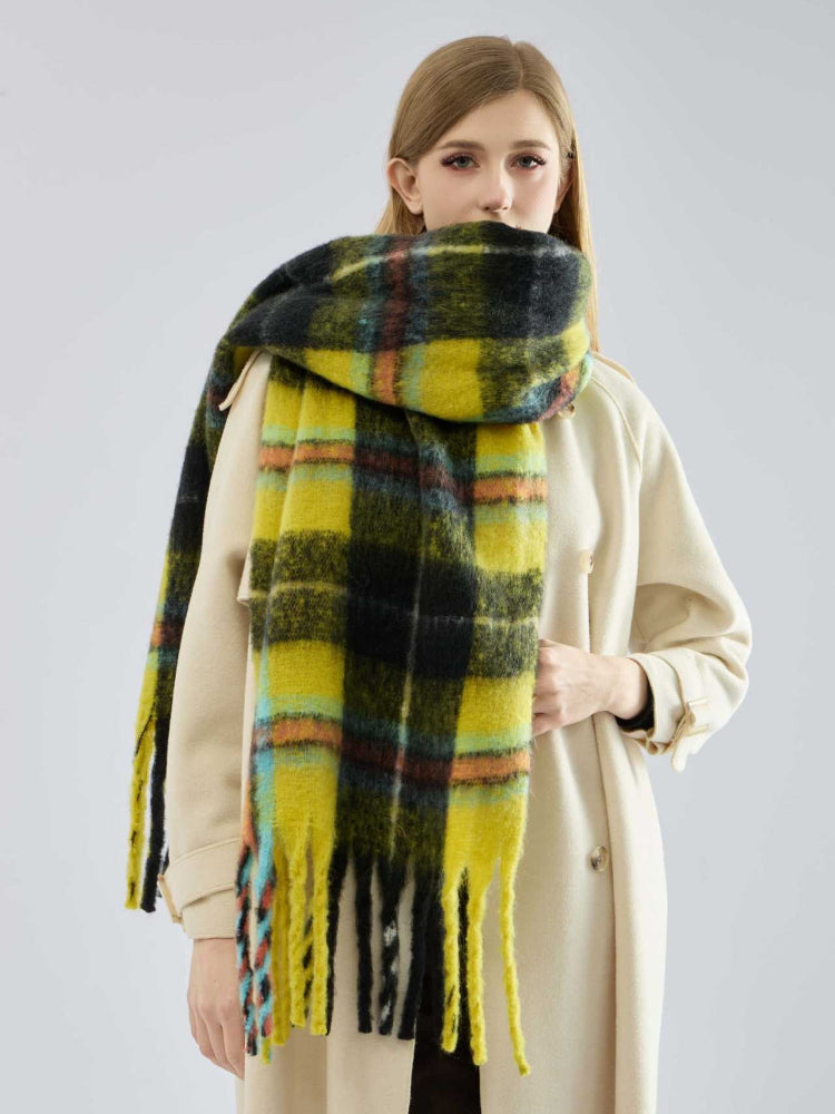 woman wearing a grey ribbed sweater and dark pants with a large plaid scarf draped around her neck