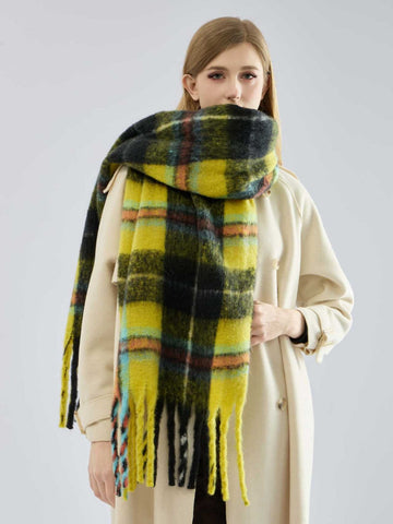 woman wearing a grey ribbed sweater and dark pants with a large plaid scarf draped around her neck