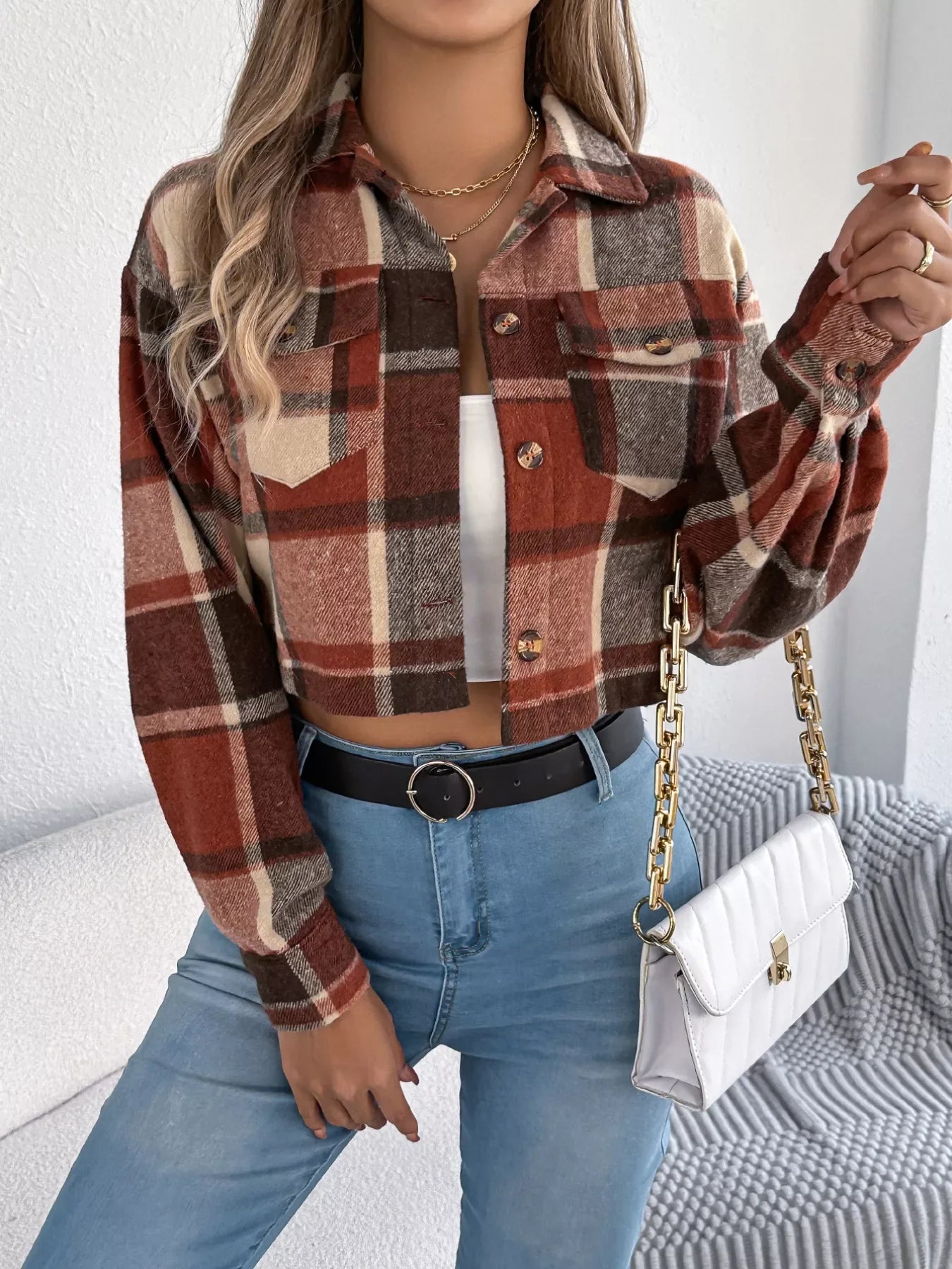 Close-up of a woman wearing a plaid cropped shirt jacket and blue jeans, accessorized with a gold necklace and a white handbag