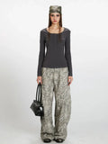 Woman wearing a dark grey long-sleeve ribbed knit top with a square neckline and buttoned placket, paired with grey leopard print wide-leg cargo pants and a black handbag.