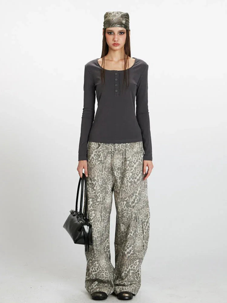 Woman wearing a dark grey long-sleeve ribbed knit top with a square neckline and buttoned placket, paired with grey leopard print wide-leg cargo pants and a black handbag.