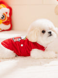 Small white dog lying down wearing a red corduroy dog vest with a cartoon graphic.