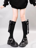 Legs of a person wearing black knee-high socks with attached plush cat figures, styled with black platform buckle shoes.