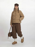 Full body shot of a woman in a tan corduroy puffer jacket with a dog print and brown pants.