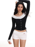 Woman wearing a black fitted long sleeve top with white ruffle trim at the neckline and cuffs, and a button-up front.