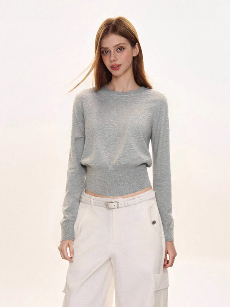 Woman wearing a light grey crew neck long sleeve cinched waist sweater