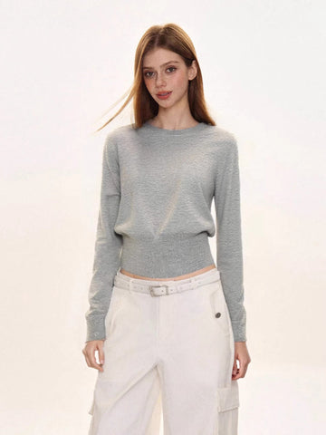 Woman wearing a light grey crew neck long sleeve cinched waist sweater