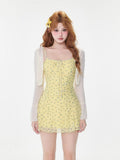 Woman wearing a yellow floral print mini dress with spaghetti straps and a tie front detail, paired with a white sheer long-sleeve shrug.