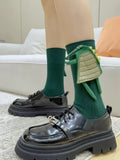 Close-up of green ribbed mid-calf socks featuring a 3D dinosaur design, worn with black lace-up platform shoes.
