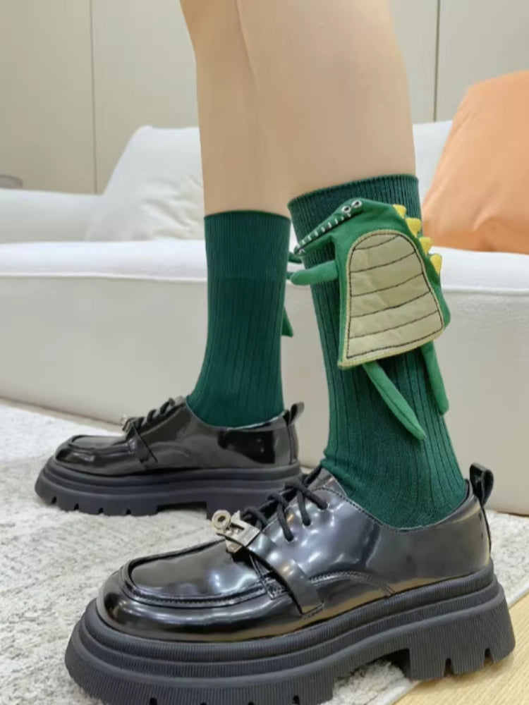 Close-up of green ribbed mid-calf socks featuring a 3D dinosaur design, worn with black lace-up platform shoes.