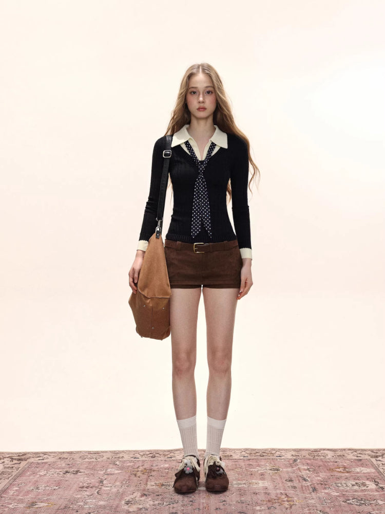 Woman wearing a black cable knit collared sweater with a white collar and cuffs, paired with brown shorts and a polka dot scarf.