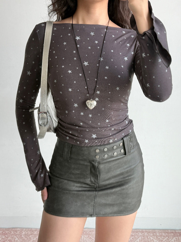 Woman with a grey star-print top, leather skirt, and a silver shoulder bag, accessorized with a heart pendant necklace.