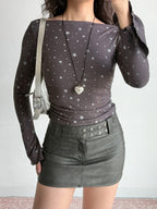 Woman with a grey star-print top, leather skirt, and a silver shoulder bag, accessorized with a heart pendant necklace.