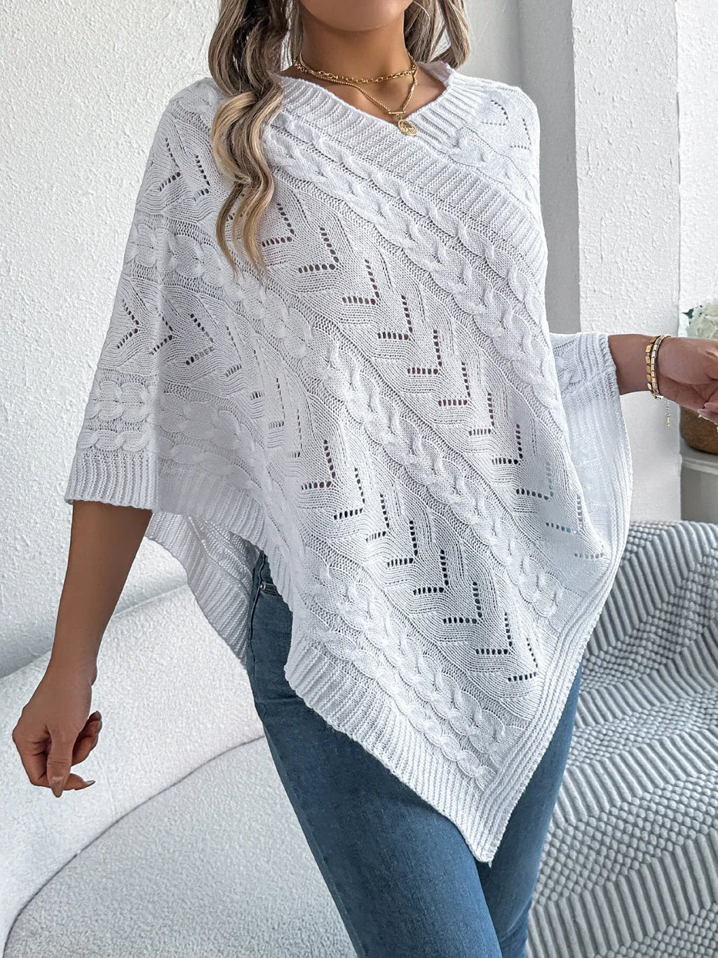 Woman wearing a white knit poncho with a V-neck and asymmetrical hem.