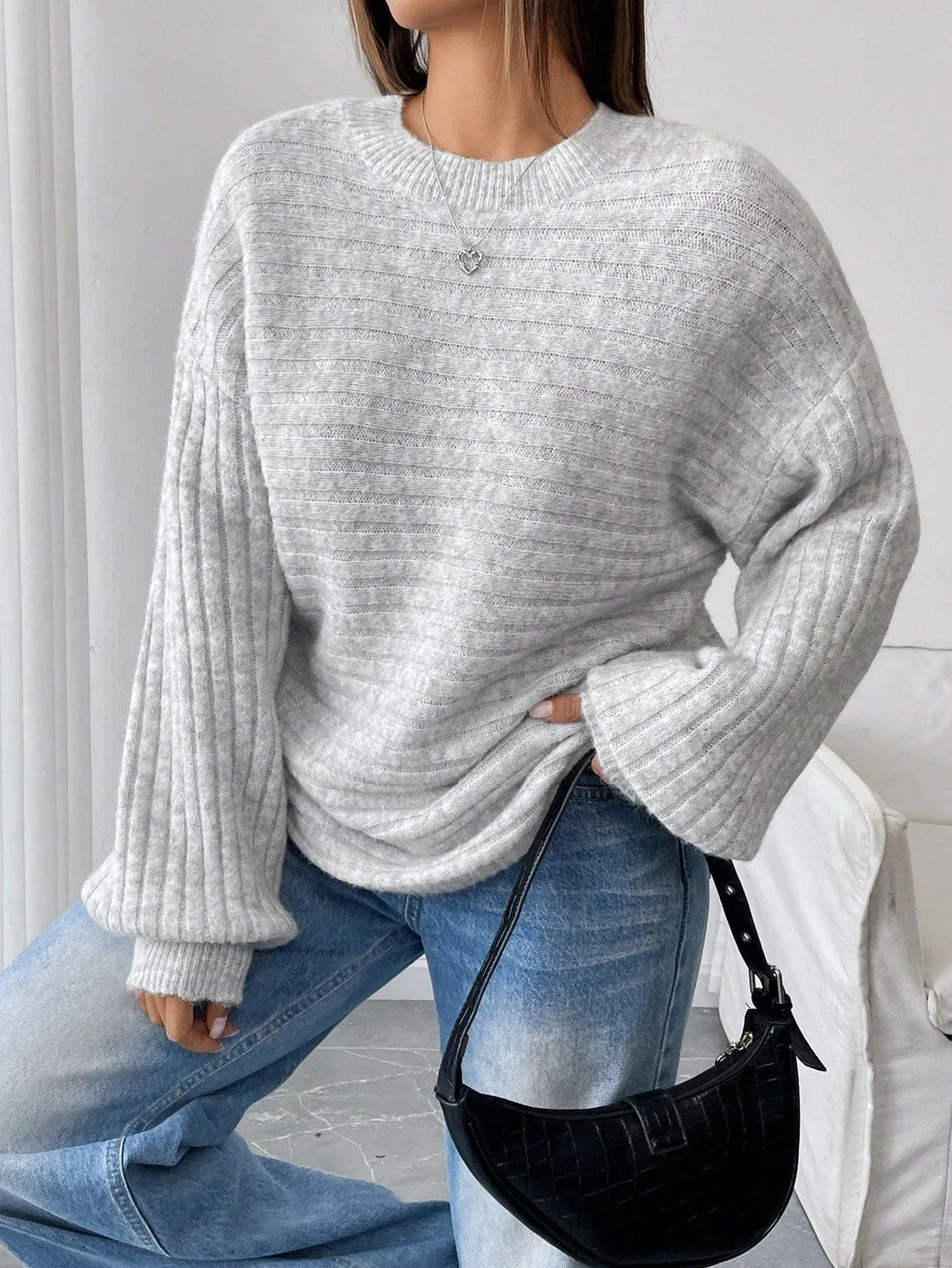 Woman wearing a light grey oversized knit sweater with long ribbed sleeves and a crew neckline, paired with blue denim jeans.