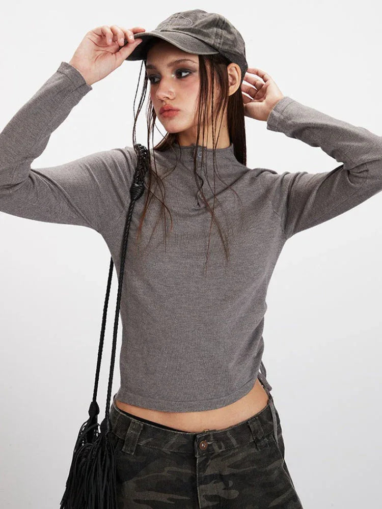 Front view of a model adjusting her grey baseball cap, wearing a grey long-sleeve mock neck cropped top and camouflage cargo pants.