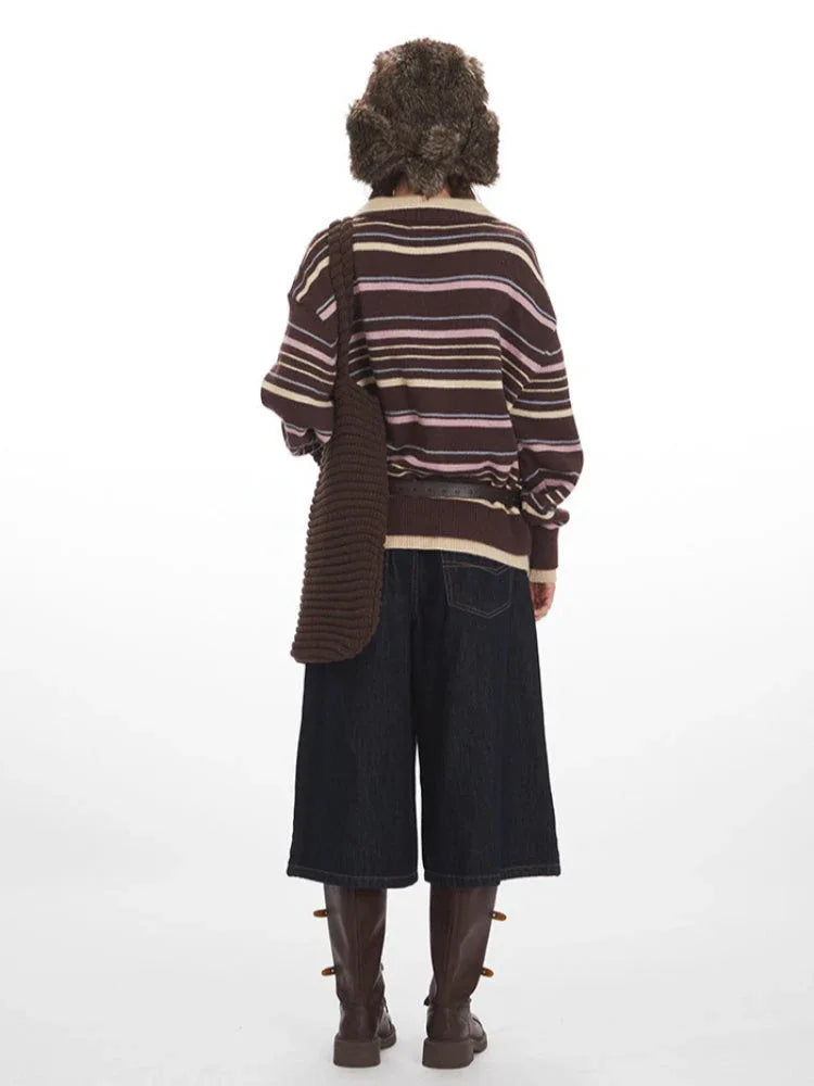 Back view of a woman wearing a brown striped knit sweater with a v-neck and collar detail, dark wash wide-leg cropped jeans, brown leather boots, a brown belt, and a brown faux fur hat with ear flaps.
