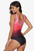 Woman in a pink and red ombre one-piece swimsuit from the back, showing criss-cross straps.