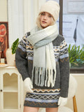 Woman posing in a knit sweater with a geometric pattern, a matching skirt, a multi-colored scarf, and a beige beanie.