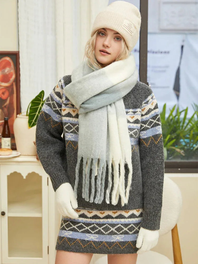 Woman posing in a knit sweater with a geometric pattern, a matching skirt, a multi-colored scarf, and a beige beanie.