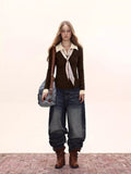 Full body shot of a woman in a brown cable knit sweater, white collar and cuffs, dark wash wide-leg jeans, and brown boots.