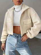 Woman wearing a cream sherpa fleece cropped jacket with a stand collar and zipper closure.