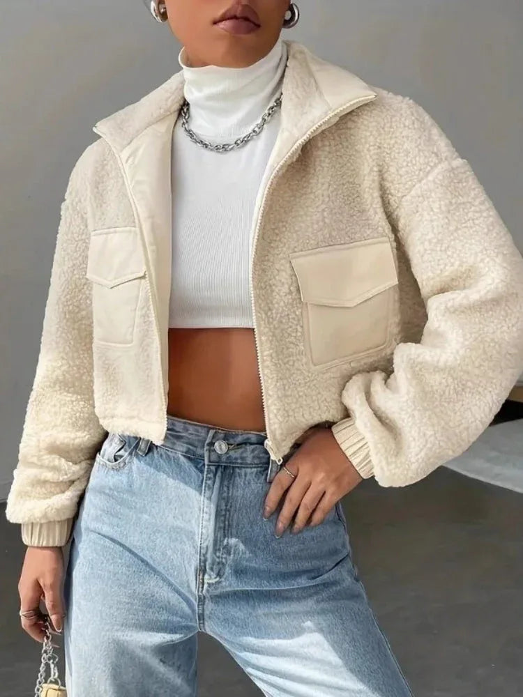 Woman wearing a cream sherpa fleece cropped jacket with a stand collar and zipper closure.