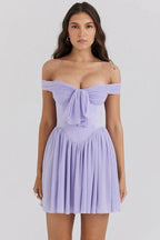 Woman wearing a light purple off-the-shoulder mini dress with a bow detail at the bust and a pleated skirt, front view.