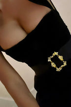 Detailed view of the neckline and belt buckle of a black velvet mini dress.