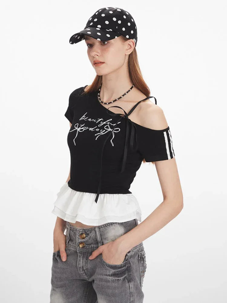 Close-up of a woman wearing a black cropped t-shirt with white graphic print and ruffle trim, featuring asymmetrical neckline with ribbon ties.