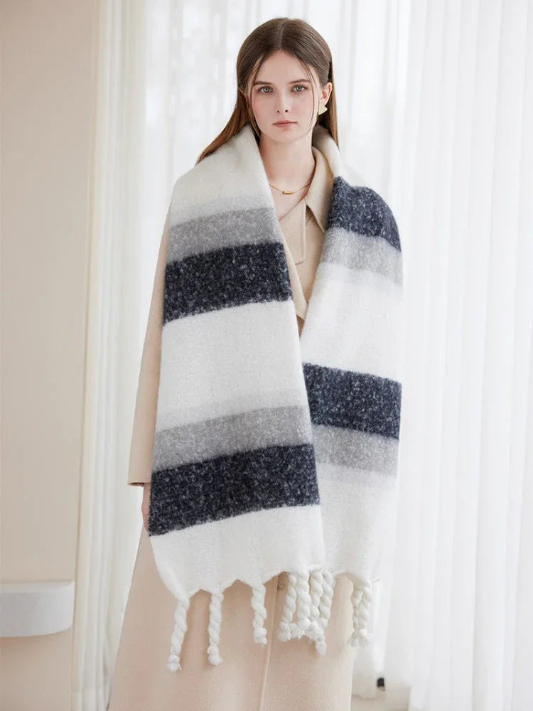Woman wearing a long, striped scarf with white, grey, and navy blue bands and white tassels