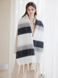 Woman wearing a long, striped scarf with white, grey, and navy blue bands and white tassels