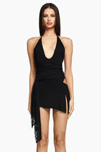 Full-body shot of a woman in a black halter neck mini dress with a V-neck and side slit.